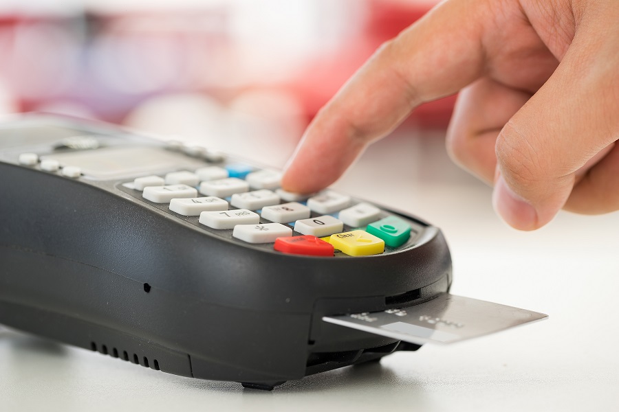 como funciona o cashback, na foto vemos uma máquina de cartão de crédito, com um cartão inseirido e um dedo de uma pessoa branco apertando as teclas